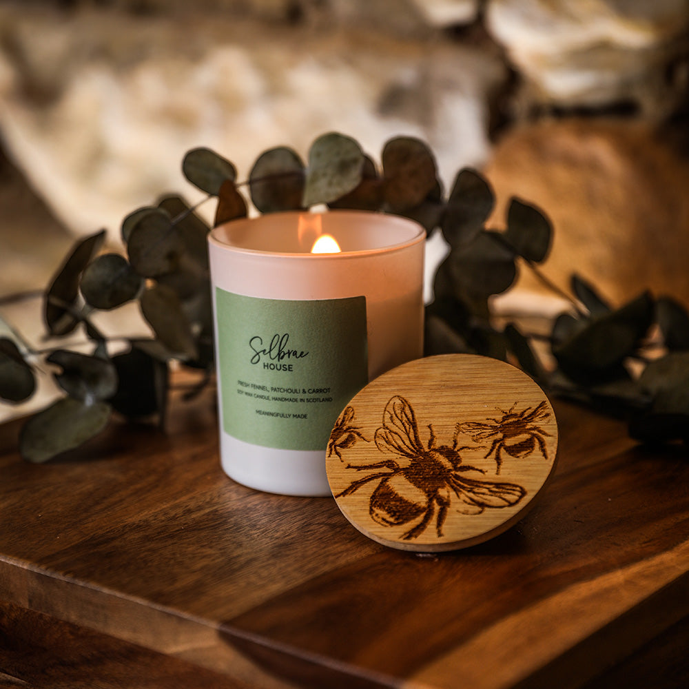 A lit bees fresh fennel candle with a green label and wooden lid engraved with bees for a fresh scent