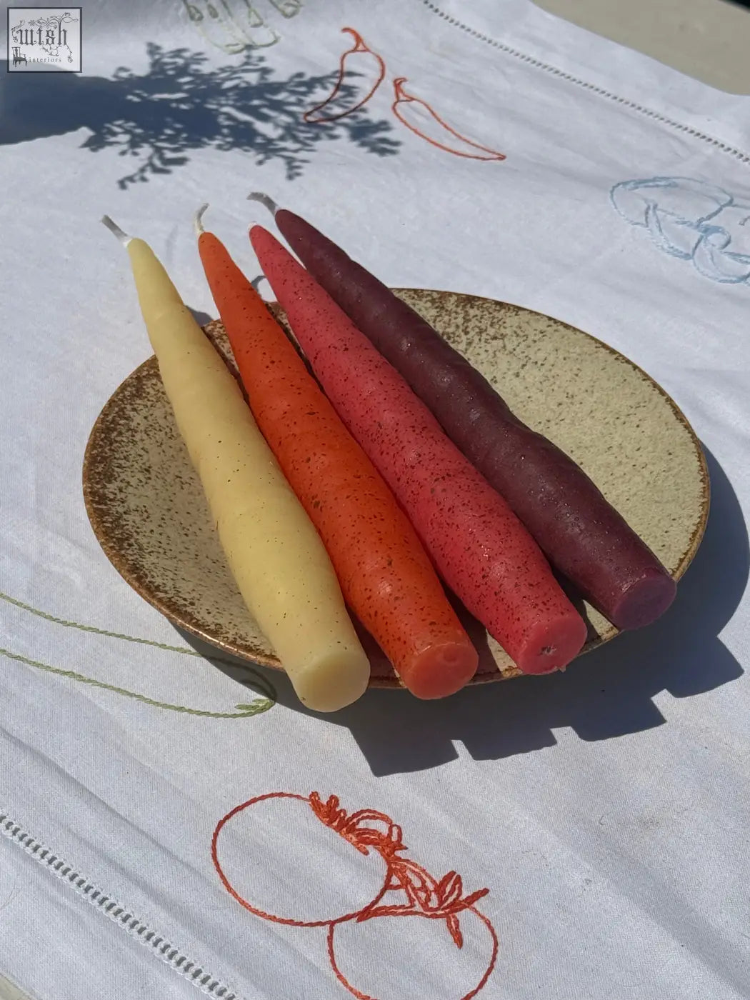 Beeswax rainbow carrot sticks pack of four tapered candles in yellow orange red and purple on a rustic ceramic plate