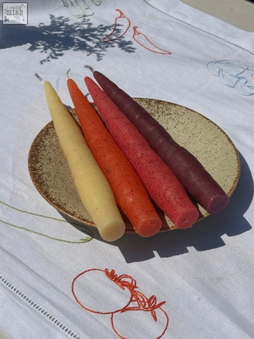 Beeswax rainbow carrot sticks pack of four tapered candles in yellow orange red and purple on a rustic ceramic plate