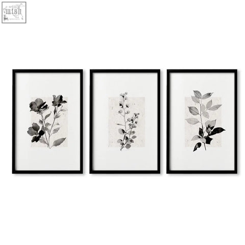 Set of three black-framed beige wall art prints with monochrome botanical pressed flower and leaf designs on textured paper