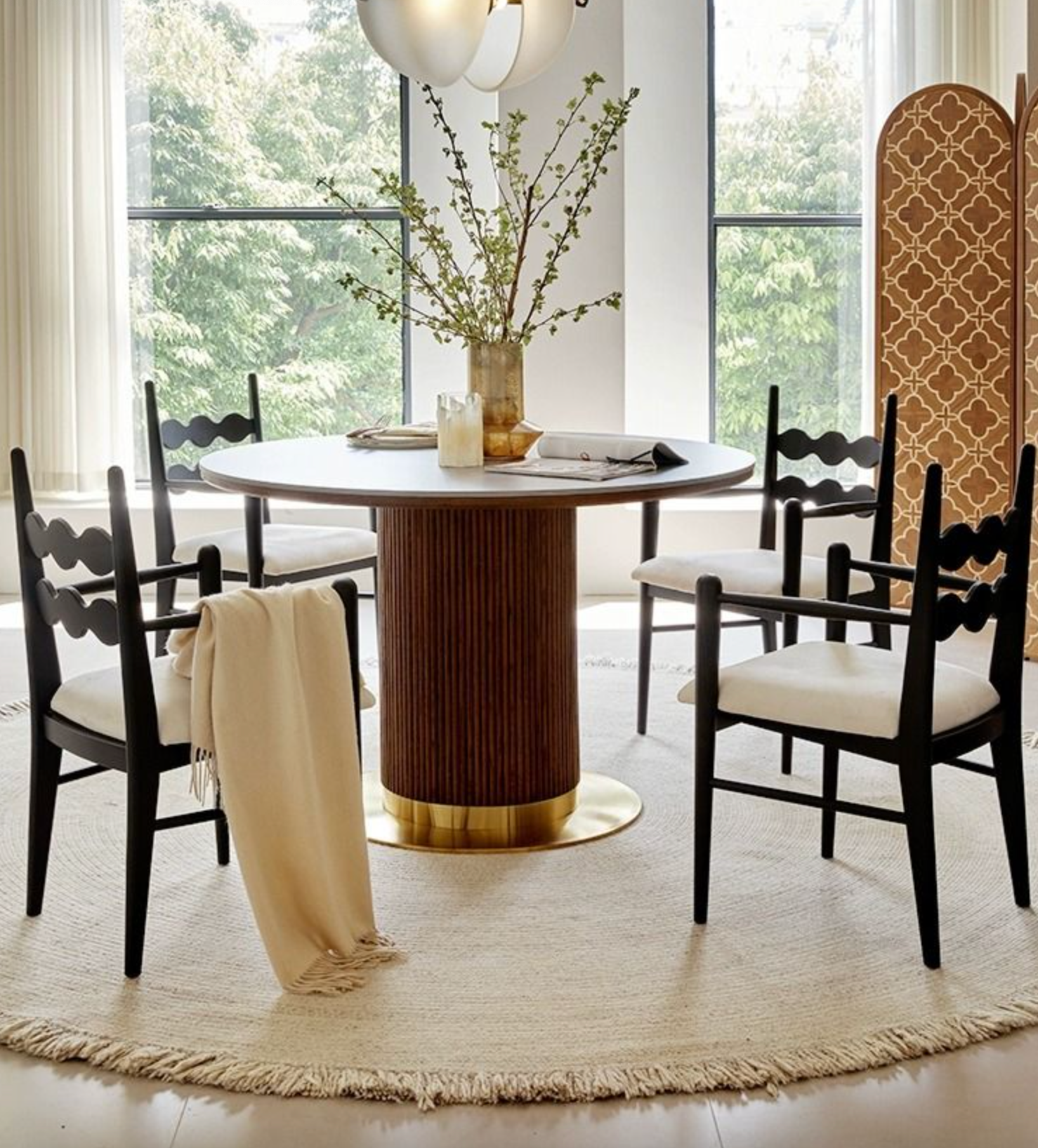 Bek round dining table in brown wood with gold-finished pedestal base and green branches centerpiece on top