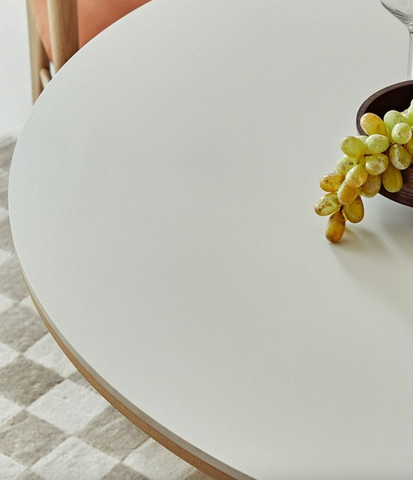 A cluster of green and yellow grapes spills from a dark wooden bowl on a white bek round dining table perfect for round dining