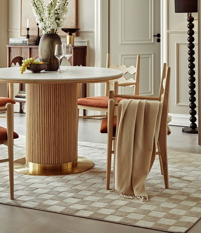 Bek round dining table with a light wood base featuring vertical grooves and a white smooth round dining surface