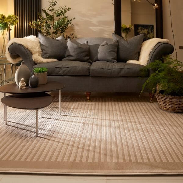 Gray upholstered sofa with rolled arms and dark gray pillows draped by cream sheepskin blanket on belgrade natural striped rug