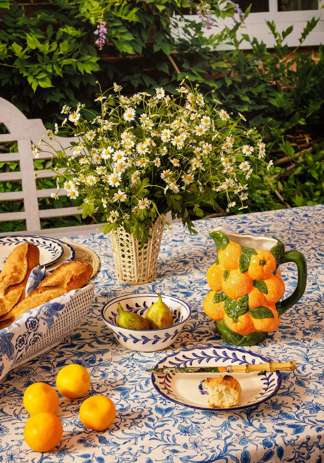 A ceramic pitcher shaped like oranges with green leaves and handle paired with belgravia bloom blue cotton tablecloth