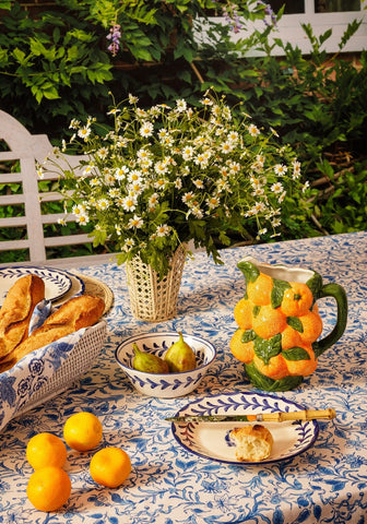A ceramic pitcher shaped like oranges with green leaves and handle paired with belgravia bloom blue cotton tablecloth