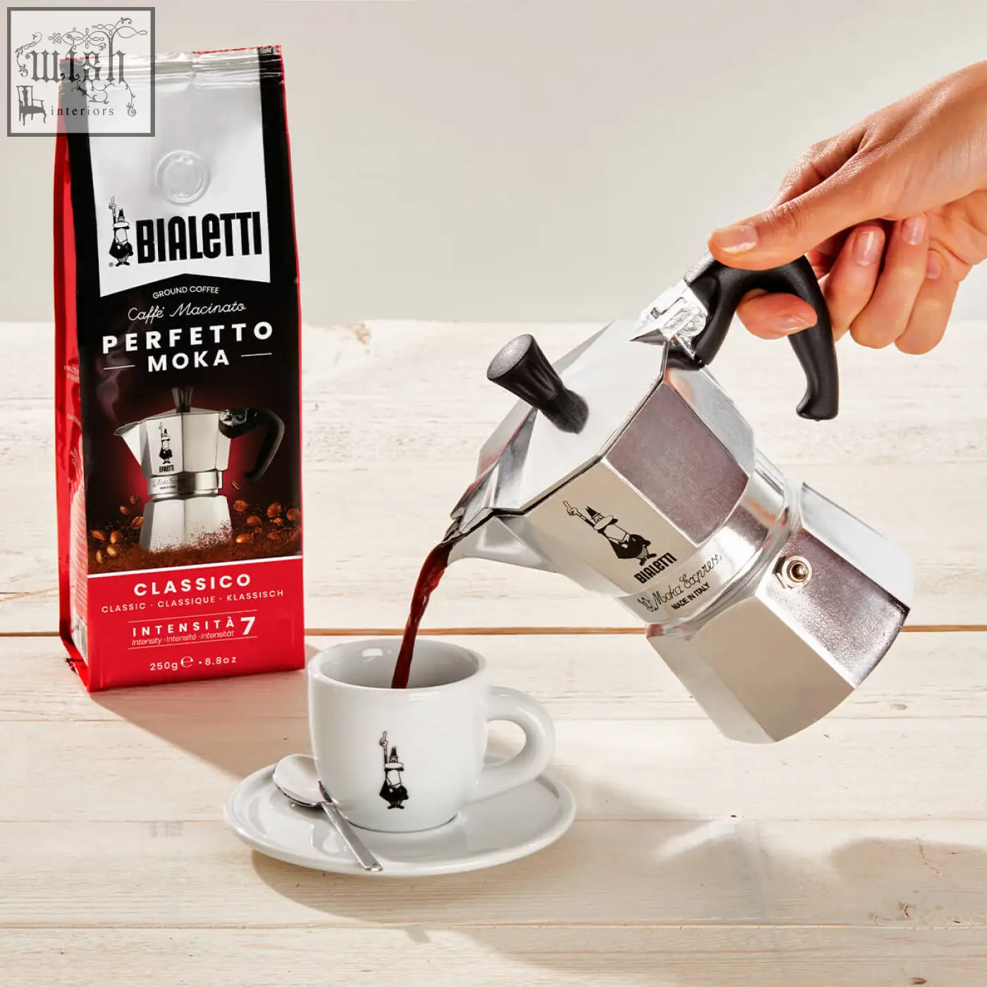 Silver bialetti moka express moka pot with black handle pouring coffee into white ceramic cup