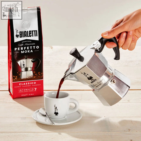 Silver bialetti moka express moka pot with black handle pouring coffee into white ceramic cup