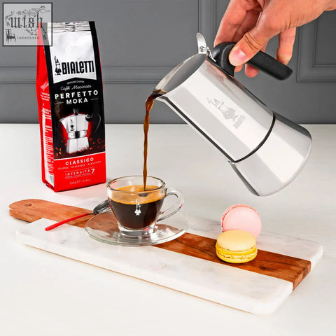 Silver bialetti venus induction moka pot pouring coffee into glass cup for rich espresso brewing