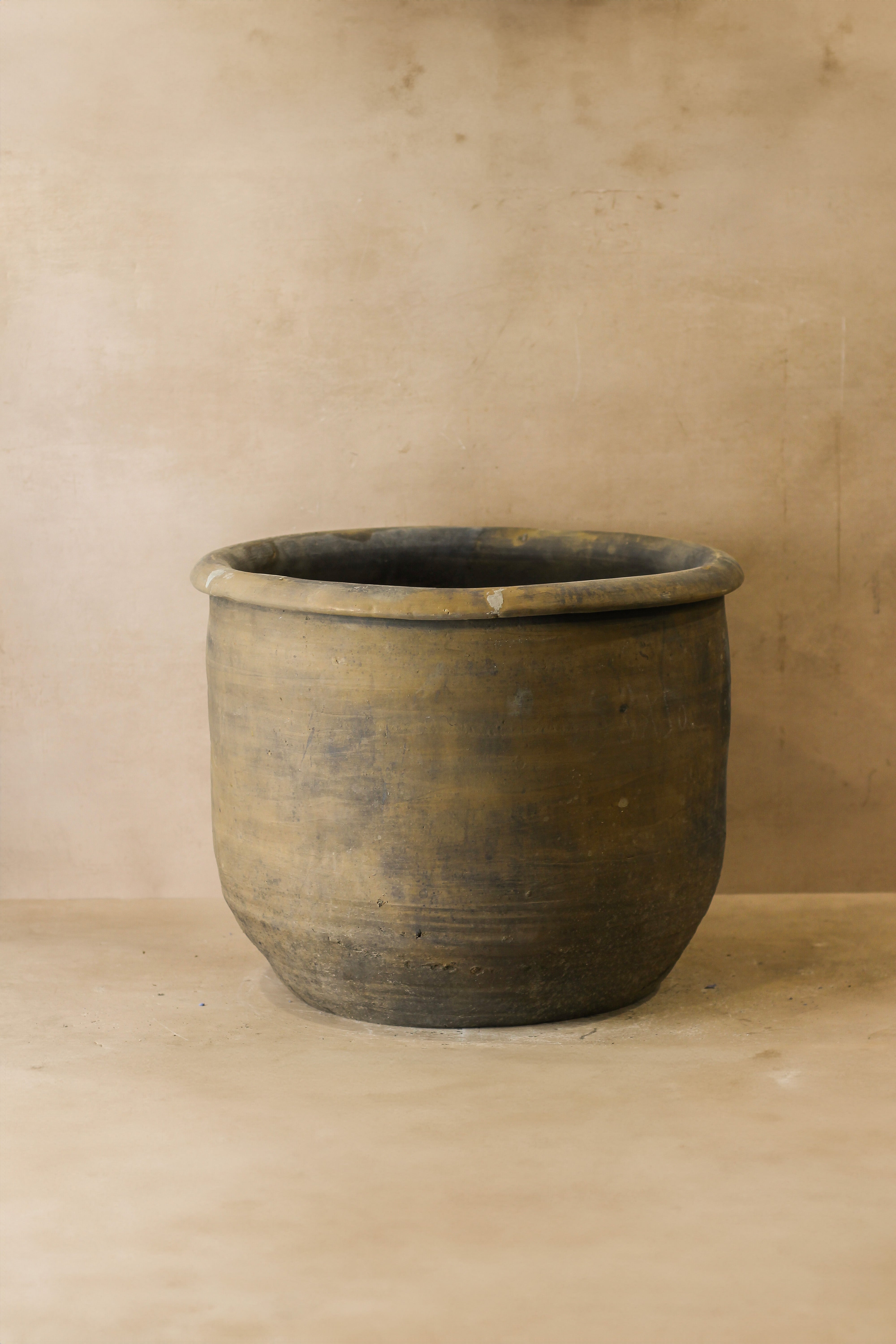 A big old grey asian pot made of rustic ceramic with horizontal ridges and a slightly chipped rim