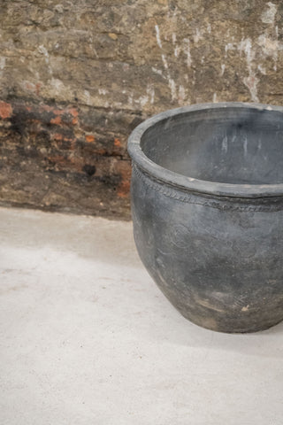 Big old grey asian pot made of dark gray weathered ceramic with subtle embossed circular patterns around the rim