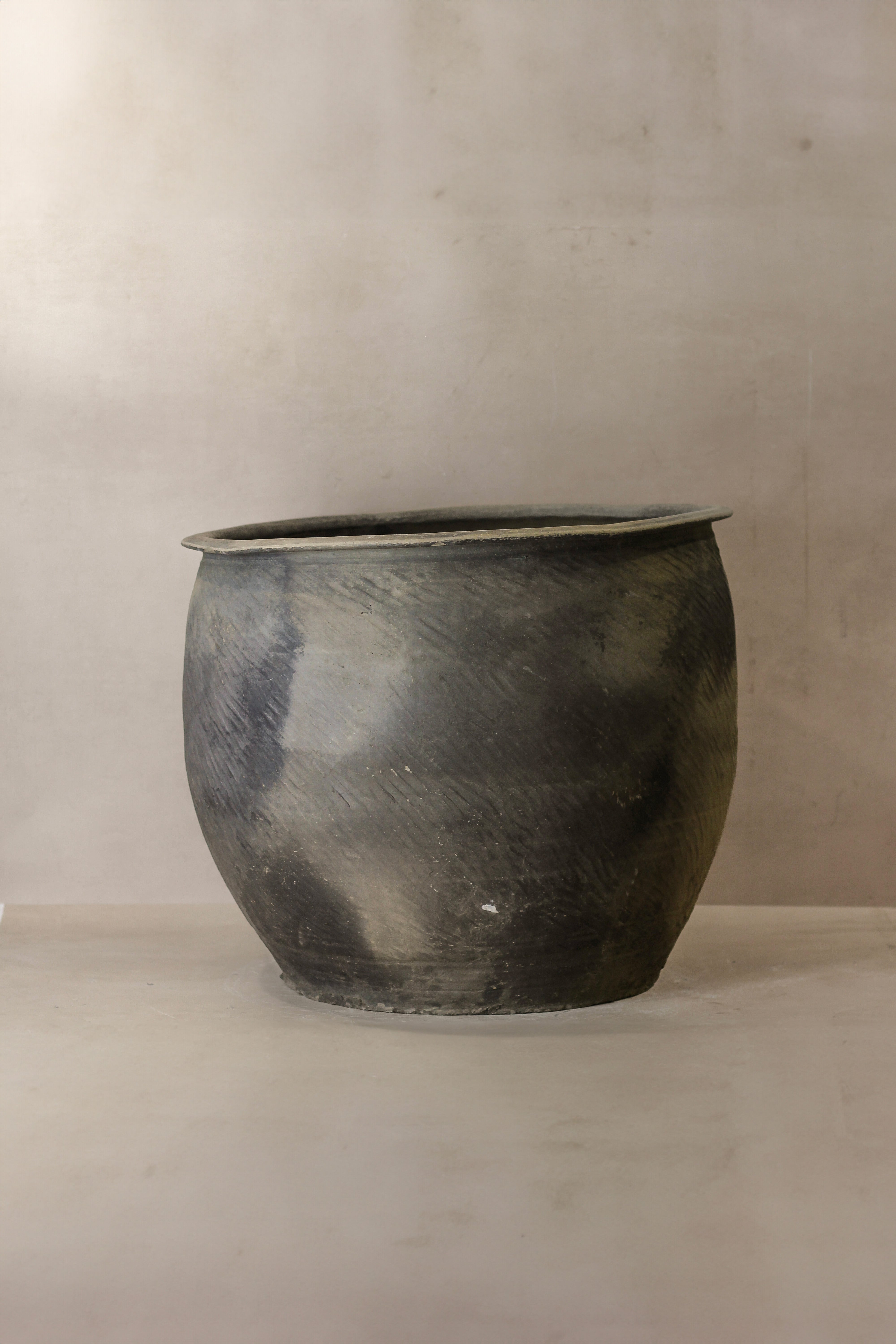 A rustic dark gray metal grey asian pot with a textured surface and slightly flared rim for outdoor use