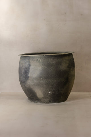 A rustic dark gray metal grey asian pot with a textured surface and slightly flared rim for outdoor use