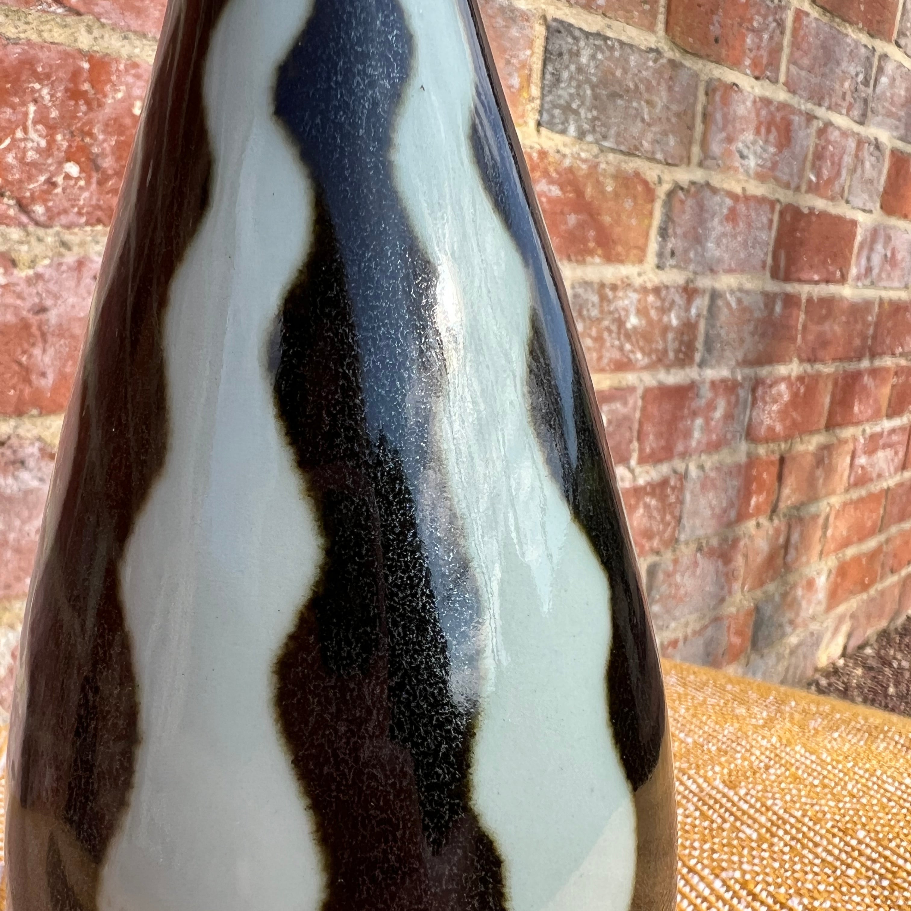 A sleek studio pottery ceramic vase with bold black and white striped wavy design and tapered shape
