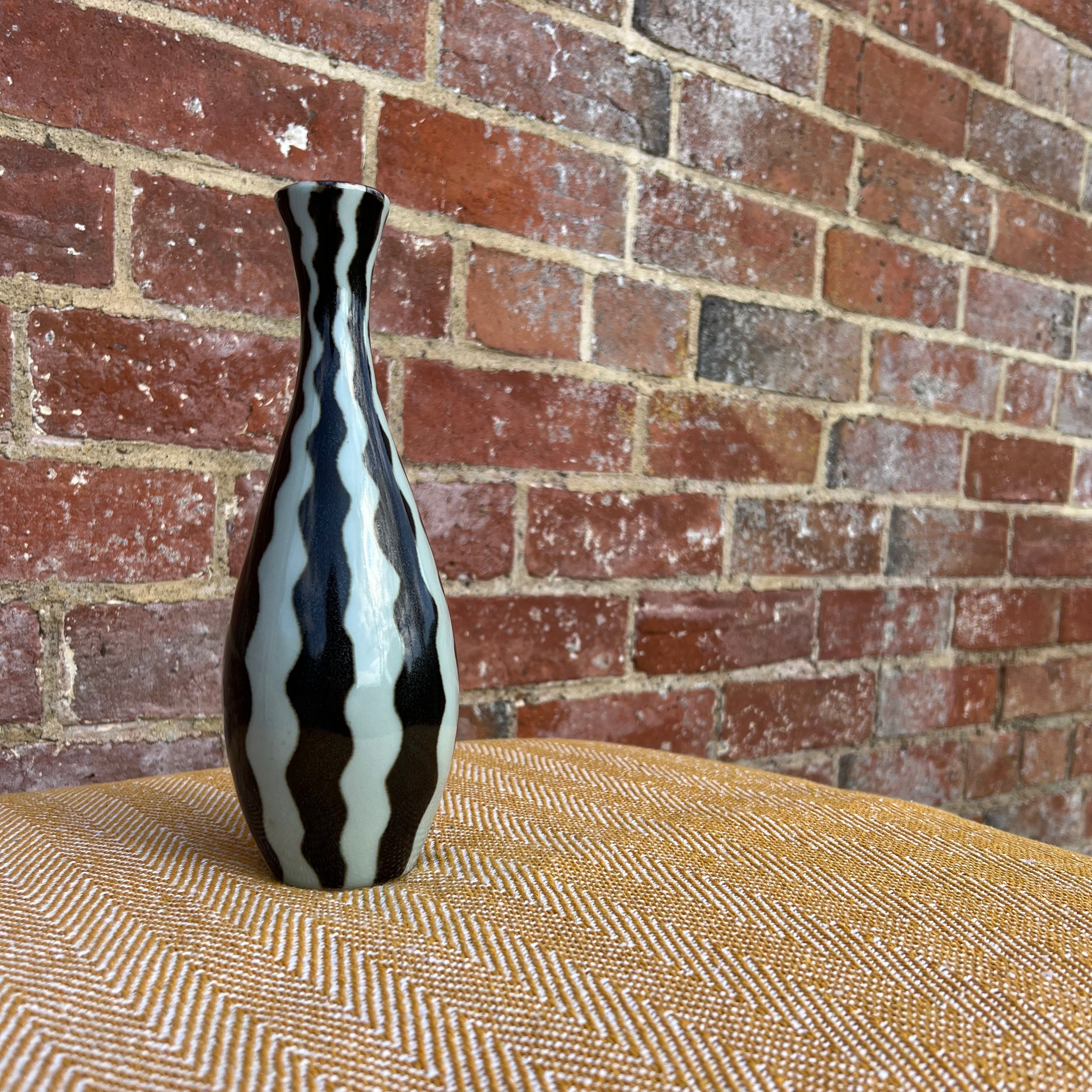 A slender ceramic studio pottery vase with bold black and white striped wavy glossy finish