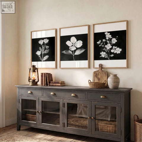 Dark gray wooden sideboard with glass paneled doors and brass handles next to black framed picture set of 3 botanical prints