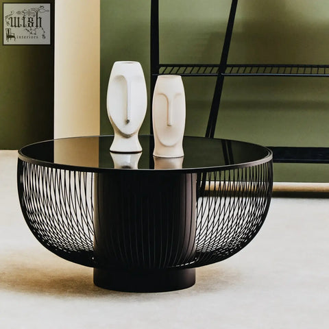 Black glass trento coffee table with matte black wireframe base and glossy top holding two white ceramic face vases