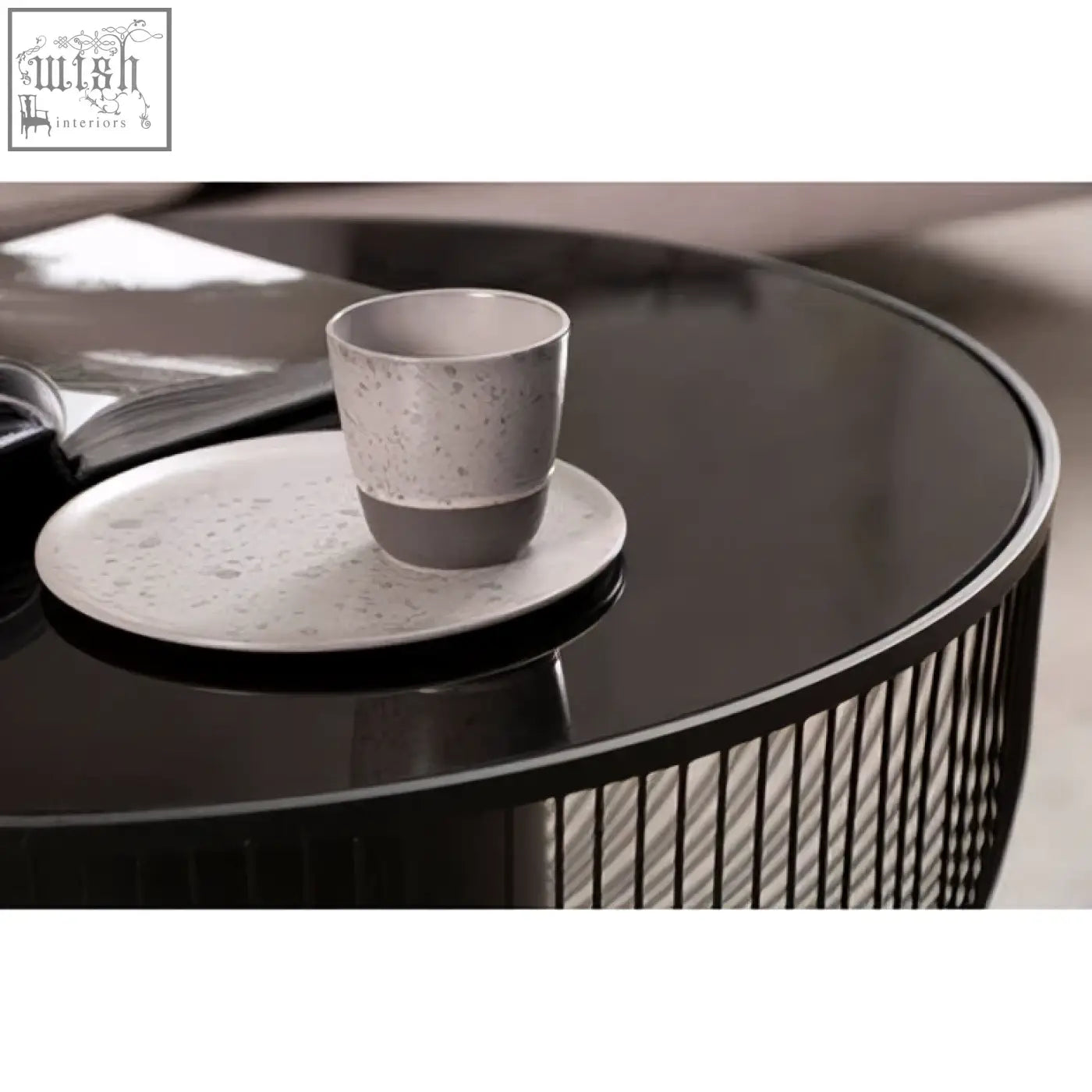 A speckled gray ceramic mug on a matching saucer on a black glass top round trento coffee table with matte black base