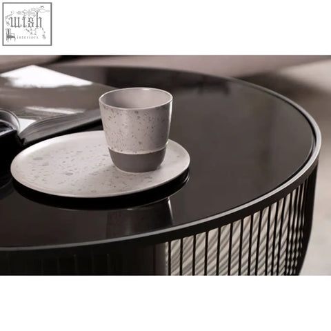 A speckled gray ceramic mug on a matching saucer on a black glass top round trento coffee table with matte black base