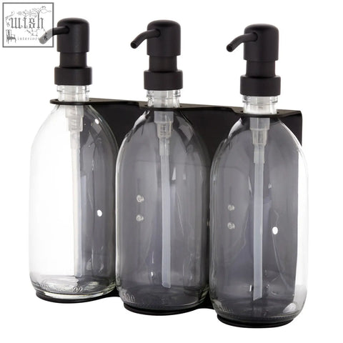 Black triple wall-mounted soap dispenser set with three transparent glass bottles and black pump tops on a sleek bracket