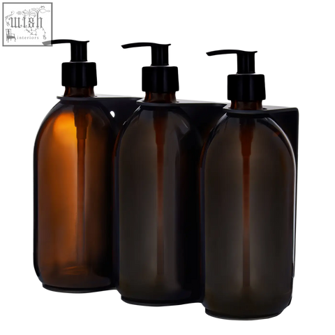Three amber glass bottles with black pumps in a wall-mounted soap dispenser for black triple use
