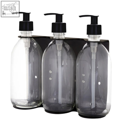 Black triple wall-mounted soap dispenser set with three transparent glass bottles and black pump heads on a sleek holder