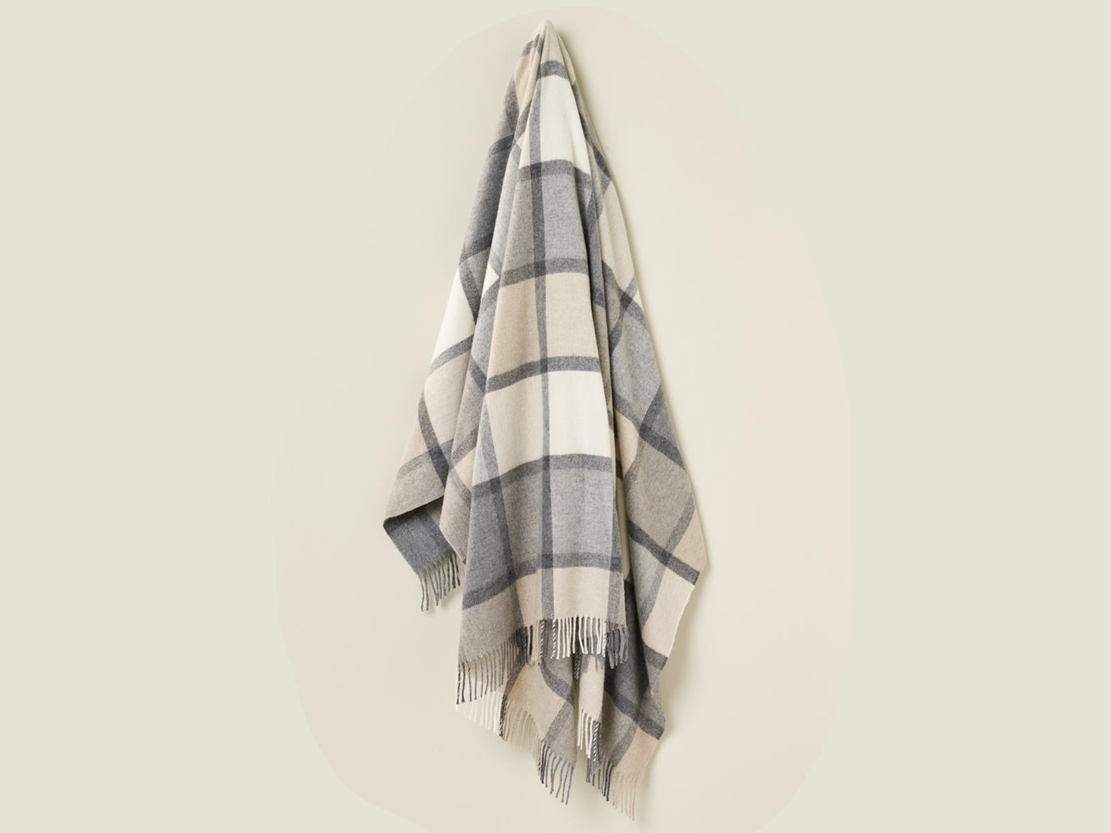 A soft cream and gray windowpane block check throw blanket made from merino lambswool with fringed edges