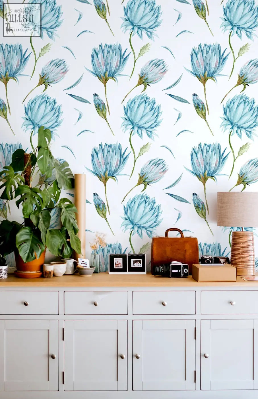 A brown leather vintage camera on wood near blue flowers wallpaper with green leaves removable wall decor by clickwalls
