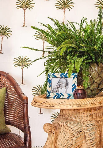 A blue geometric photo frame 6x4 sits on a wicker table next to a vibrant green fern in a textured pineapple pot