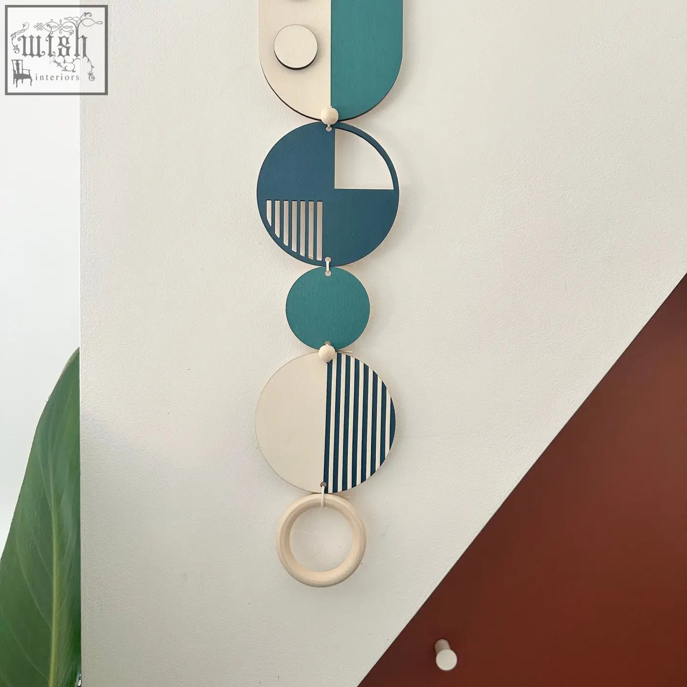 A modern wall art piece with teal cream and navy blue layered discs connected by wooden beads and a natural wood ring