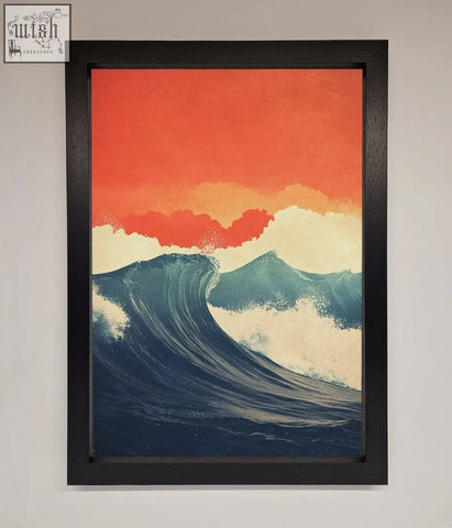A framed poster of blue waves crash under a red sunset with an orange sky in a sleek black frame