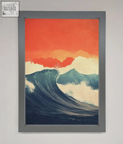 A framed poster of blue waves crash under a red sunset with an orange and cream sky in a sleek gray frame