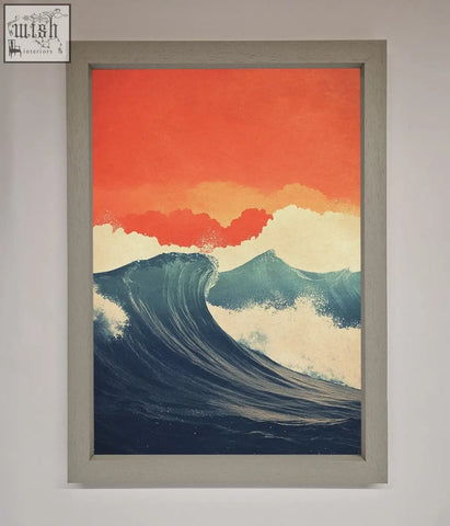A framed poster showing blue waves crash under a red sunset sky in a light gray wooden frame
