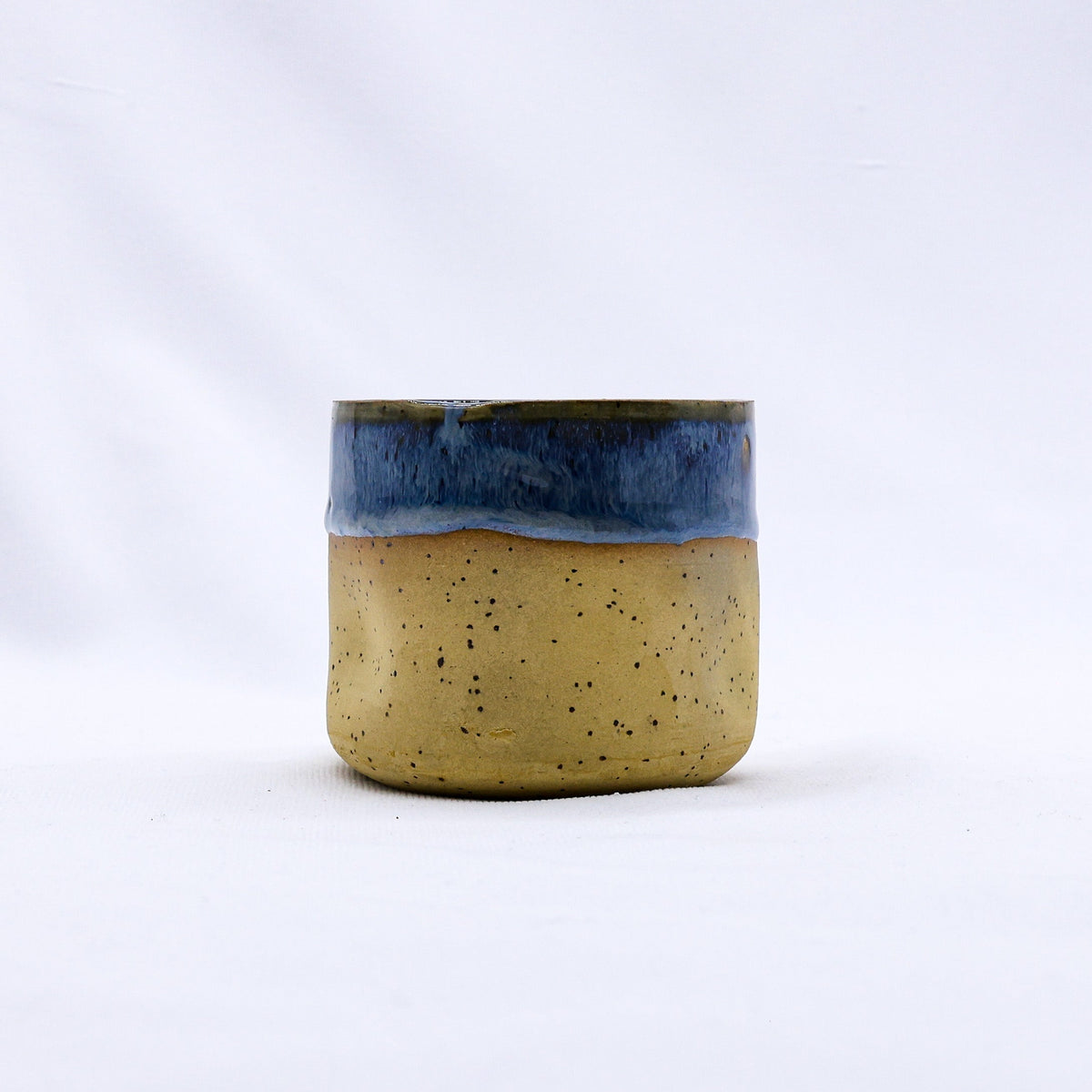 A bluvia goccia handmade ceramic stoneware cup with a speckled tan body and vibrant blue glazed rim