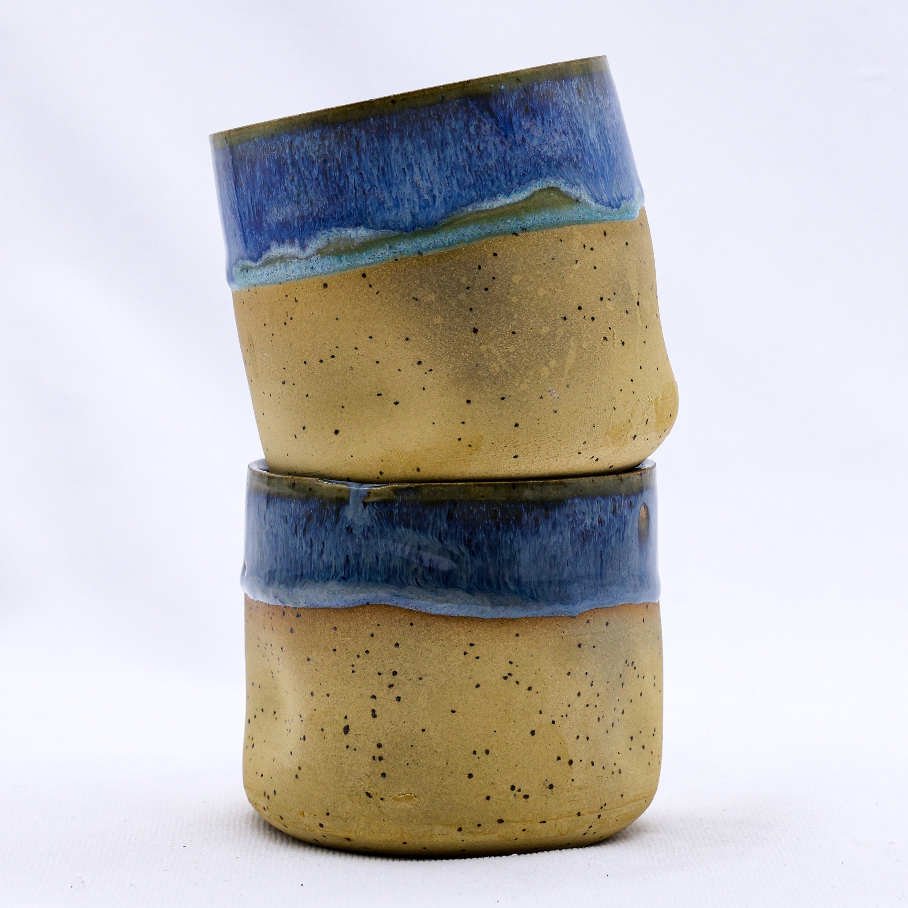 Two stacked bluvia goccia handmade ceramic stoneware cups with speckled tan body and vibrant blue glazed rim