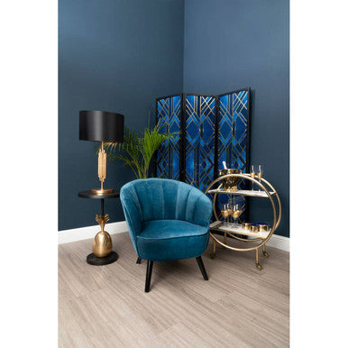 Velvet teal armchair with black legs placed next to a boho pineapple table with carved wood details