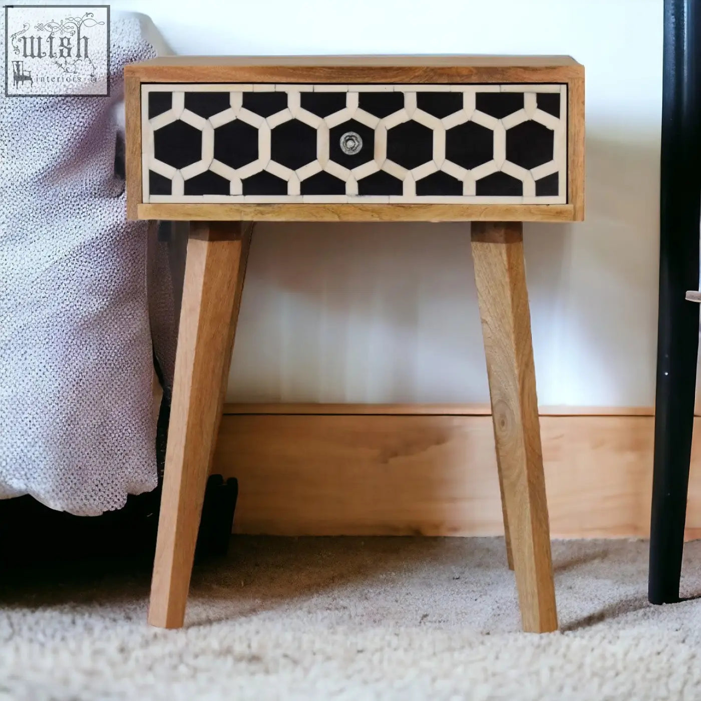 A sleek tapered bedside table with black and cream bone inlay on solid mango wood and angled legs