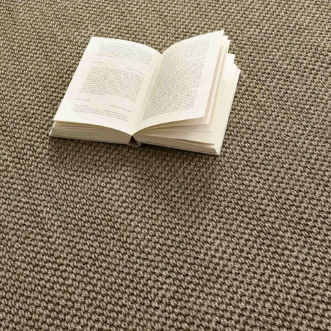 An open book rests on a bordered sage green non slip sisal rug with a textured neutral tone surface