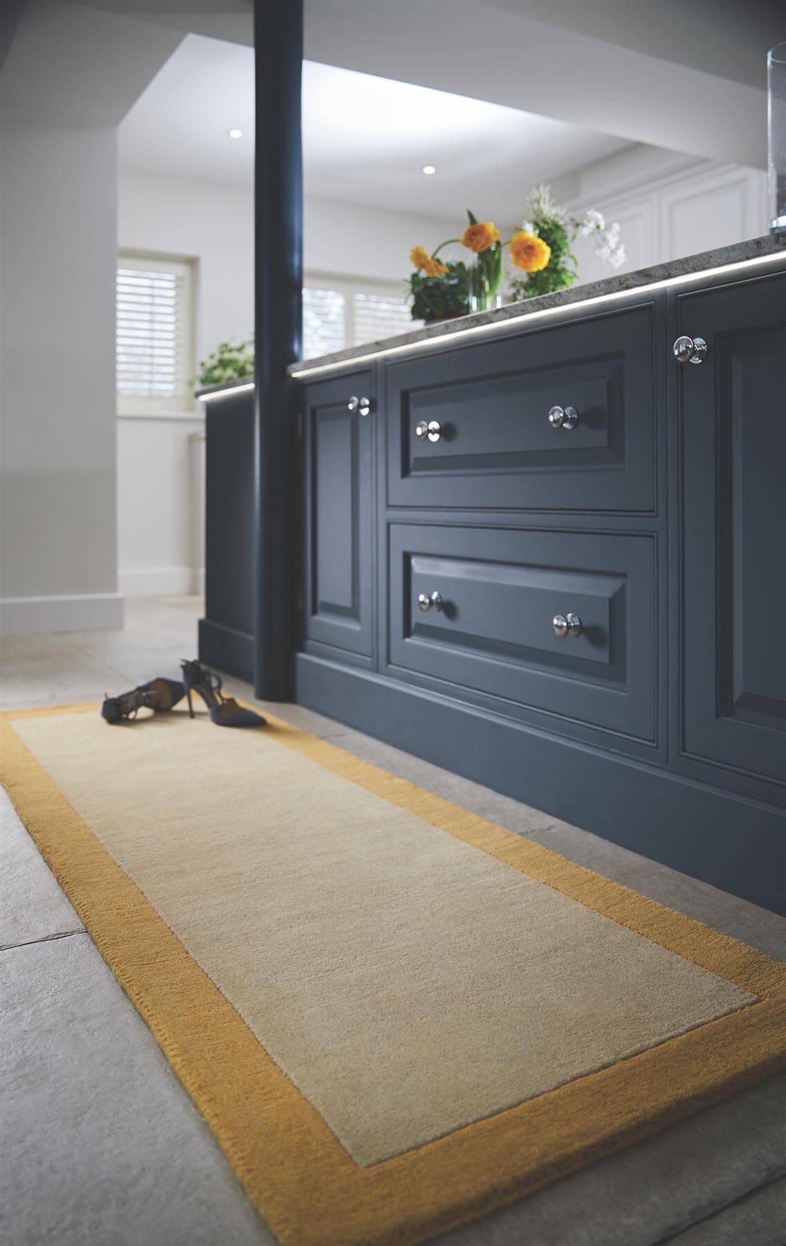 Beige bordered yellow wool rug with mustard yellow border placed beside dark blue kitchen cabinets on the floor