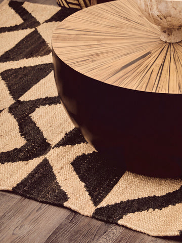 A sleek modern coffee table with a glossy black base and sunburst wooden top on a bosie hemp large rug