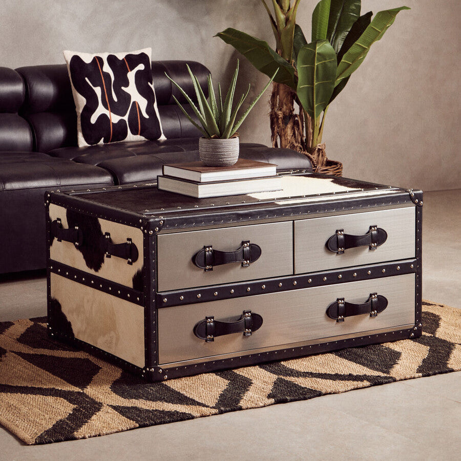 A rustic coffee table with black and silver metal finish and leather handles next to a bosie hemp small rug