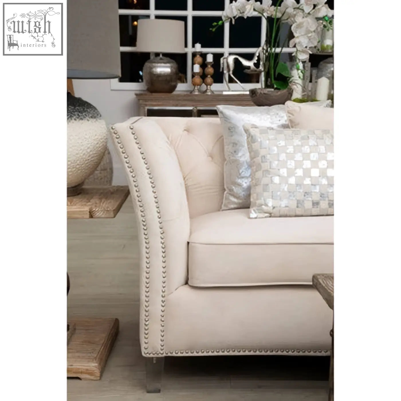 Cream-colored tufted sofa with nailhead trim and metallic legs paired with ivory silver cushion