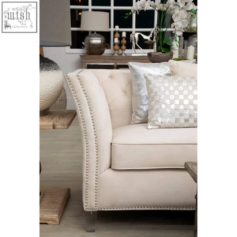 Cream-colored tufted sofa with nailhead trim and metallic legs paired with ivory silver cushion