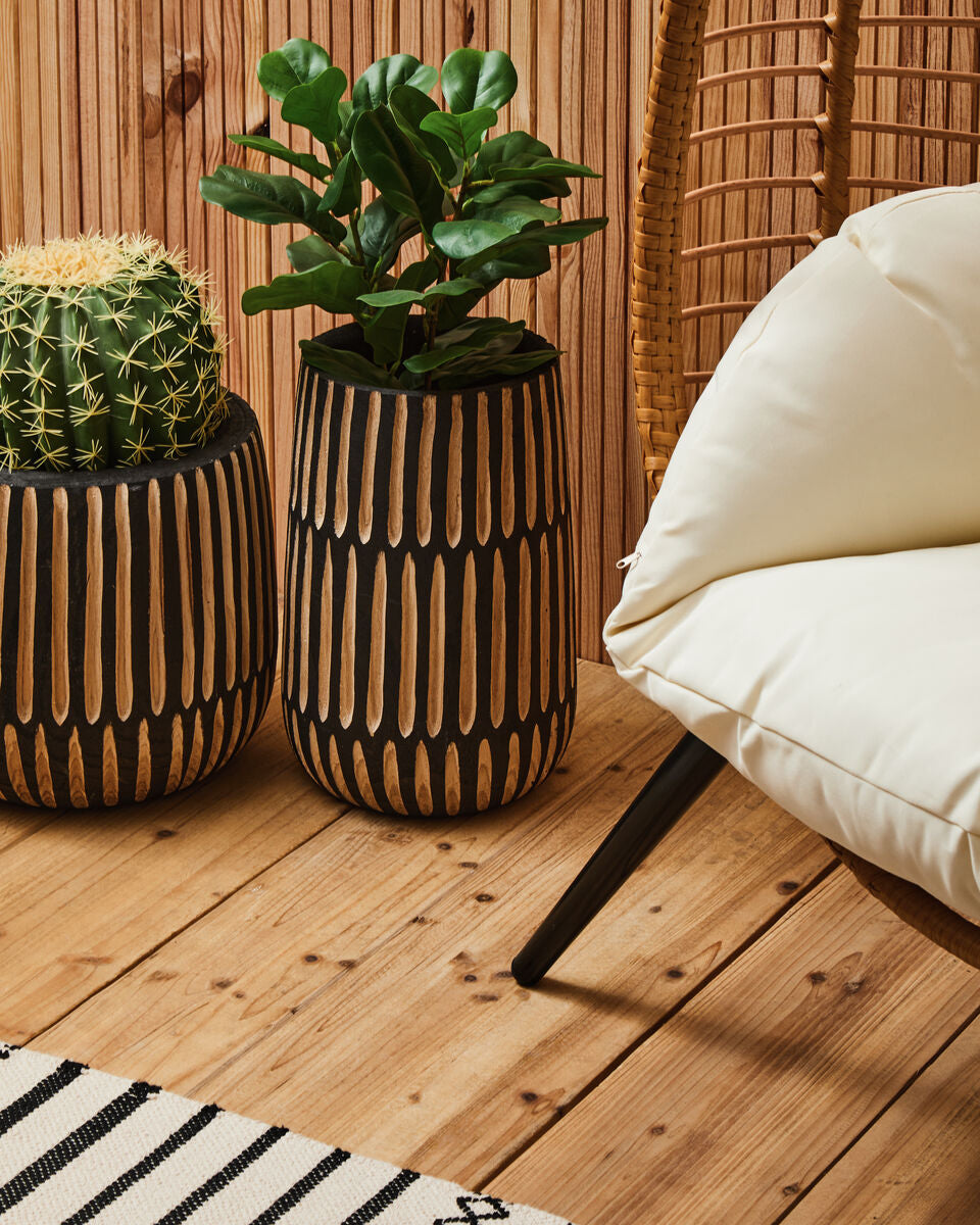 Two cylindrical wood-grain planters with black accents holding green plants next to a bosie madras premium cotton dining runner