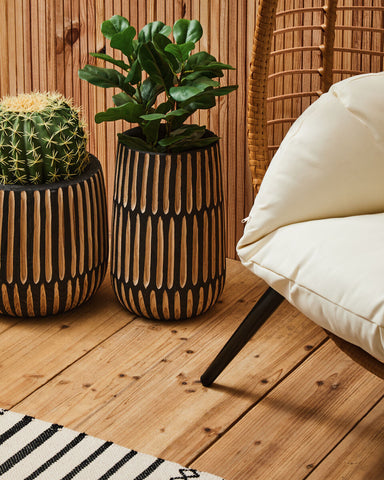 Two cylindrical wood-grain planters with black accents holding green plants next to a bosie madras premium cotton dining runner