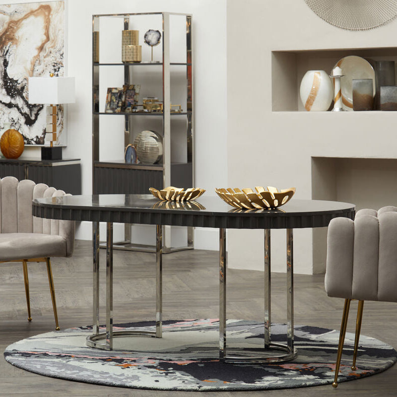 Black oval dining table with sleek reflective surface and slender chrome legs shown on bosie moyo round rug