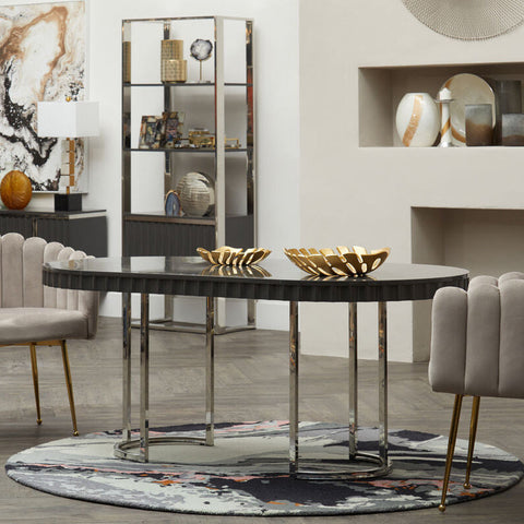 Black oval dining table with sleek reflective surface and slender chrome legs shown on bosie moyo round rug