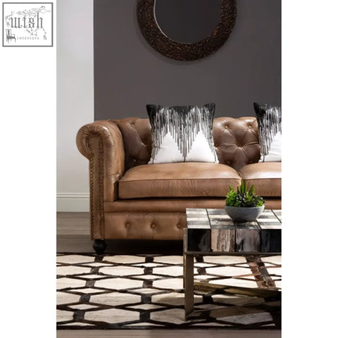 Brown leather tufted sofa with rolled arms and nailhead trim featuring bosie ozella black and white embroidered cushion
