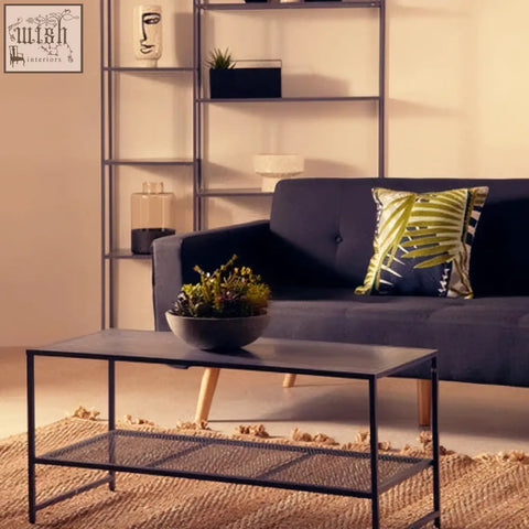 Black metal coffee table with glass top and lower shelf paired with a botanical green cushion for stylish seating