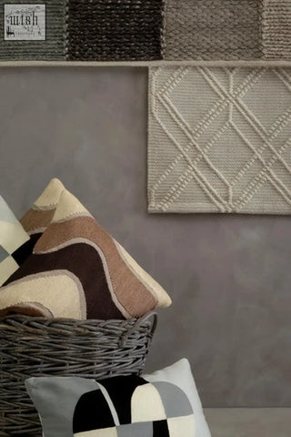 Beige knitted throw pillow with diamond pattern in woven basket beside other pillows from bosie ozella circular print collection